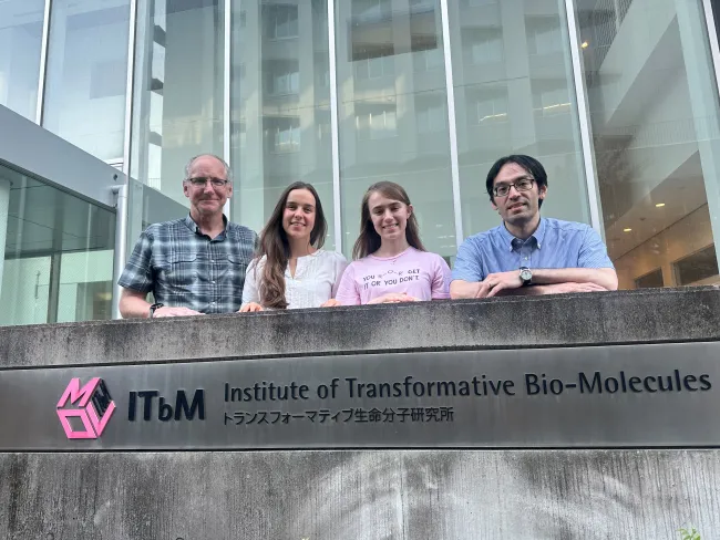 David Forbes, Bailey Baxter, Mary Helene Marmande and Masakazu Nambo stand behind the Institute of Transformative Bio-Molecules sign outside its glass-fronted building at Nagoya University, Japan.